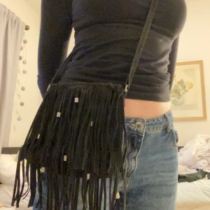 Handväska  - Väska med fransar och magnetlås. Väskan är väldigt rymlig och banden är justerbara så man kan välja om man vill ha den cross-body eller bara på ena axeln!💞 