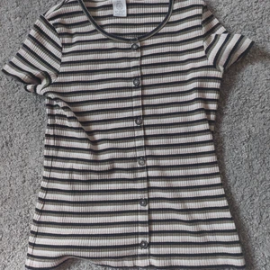Randig t-shirt från Lindex str 146/152 - Använt ca 5 gånger. Randig t-shirt från lindex med knappar som ej går att knäppa upp där fram. 