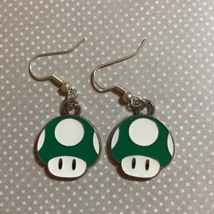 Super Mario Örhängen Grön - Nya Super Mario inspirerade örhängen, perfekt till Nintendo älskaren! Svampen är ca 1,6cm som störst. Föredrar Swish, skickar bara och möts ej upp helst.