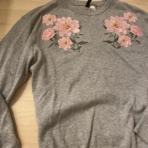 grå tröja  - en jätteskön tröja med blomdetaljer. Inga skador eller defekter. Storlek M men sitter skönt och bra på mig som har S.