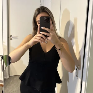 Svart linne med volanger - Superfint svart linne med V-urringning och volanger vid midjan.  Använd några gånger men bra skick! 