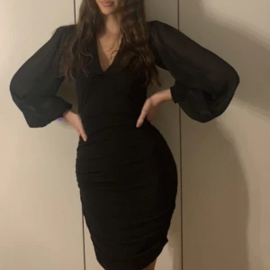 Svart festklänning  - Svart kort festklänning med långa puffiga ärmar, rychad vid sidorna