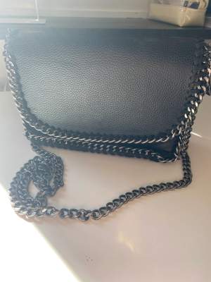 En svart väska med en metalkedja, väskan är i gott skick och knappast använd. 