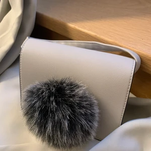 Handväska  - En grå handväska med fluff detalj på. Axelrems band sitter på. 