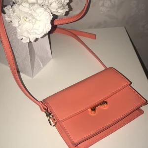 Helt oanvänd mini väska från Åhlens  - Helt oanvänd mini väska från Åhlens i en corall förg med guldiga detaljer. Har också en fick för kort 🤍 Orginalpris kring 300-400kr ( kommer ej ihåg ). 🤍