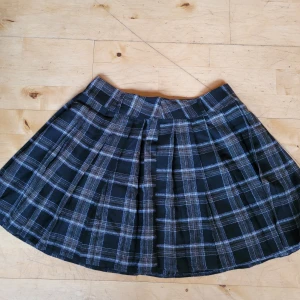 Rutig kjol  - Säljer en fin rutig kjol! Helt ny då den var för liten. Svart i botten med vitt och brunt. Storlek L, 40 cm rakt över midjan. Kan troligtvis passa en större M också. Säljer för 80 kr, frakt tillkommer med postens spårbara! 