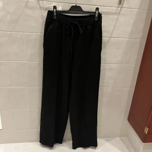 Svarta glättade kostymbyxor  - Svarta glättade kostymbyxor från Zara. Loose-fit och utsvängda/raka + vida i modellen. Snörning upptill. Storlek xs men passar även S. Skriv för fler bilder!