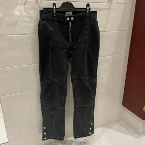 Svarta Jeans med lappteknik och knappdetaljer - Unika Svarta jeans från Weekday med lappteknik och knappar nedtill som går att knäppa och knäppa upp till en mer bootcut modell. Sitter supersnyggt! Bra skick. Storlek 36. Skriv för fler bilder!