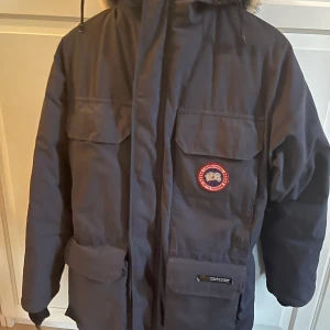Canada goose jacka - Säljer en gammal canada goose jacka som har använts av min förälder. Den är lite trasig i nere vid handen(kolla bild 3) annars inga skador. Är lite osäker på vad storlek är men tror de står xs men den passar mig som är typ 1,80 lång