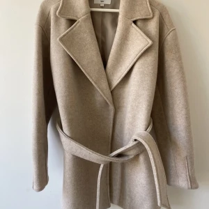 Beige kort Kappa NA-KD  - Kort kappa från NA-KD i färgen beige. Storlek 36. Väldigt fint skick! Skickar spårbart för allas trygghet😊 Köp plagget genom att trycka på ”köpknappen” men har du frågor går det bra att kontakta mig här💞