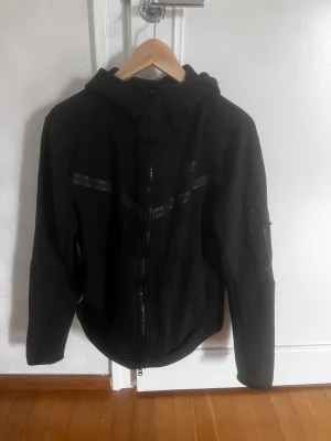 Nike Tech Fleece Tröja  - Säljer min Nike tech fleece tröja som är svart. Köpt av min kompis därav har jag inget kvitto, cond 7 av 10 då den är använd. Sedan kan ni se på bild tre att en av knapparna har lossnat. Vid minsta fundering hör av dig! 