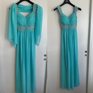 Turkos Balklänning - En superfin klänning jag hade som balklänning och då endast använd en gång! Den är i mycket fint skick! Man får med en liten sjal som man kan ha över axlar eller liknande om man vill. Klänningen är hellång. Bak i ryggen är det smock som gör att den passar fler! I klänningen står det att det är storlek ”6” men jag gissar på att storleken är ca en xs/s. Skriv till mig om ni vill ha mer bilder på den, skulle möjligen kunna leta upp bilder när jag har den på mig då jag inte kommer i den nu.