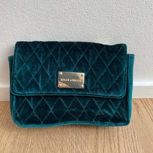 Holly&Whyte dark green i sammet väska - Det är en axelremsväska från Holly&White. Materialet är sammet och färgen är mörk grön. Den har inga fläckar på sig men guldbrickan är lite repig men det är inte synligt. Axelbandet är guldkedjor och väger inte så mycket heller. 