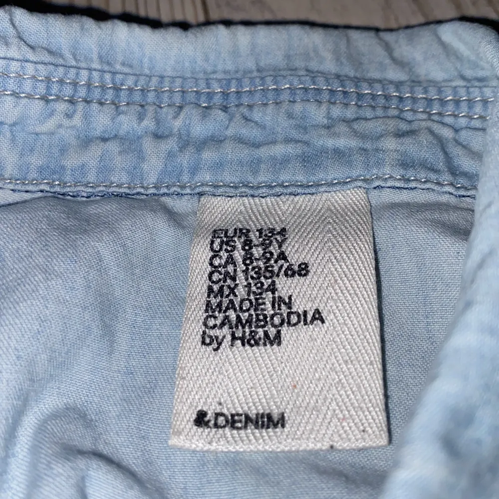 Ett enkelt ljusblått jeans-linne med knappar och 2 små fickor, gott skick. Jeans & Byxor.