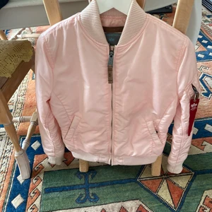 Alpha Industials jacka - Ljusrosa vår/sommar jacka ifrån Alpha i deras älskade bomberjacka. Väldigt lite använd, hel och fin, perfekta vårjackan egentligen då den tål lättare både regn och vind!