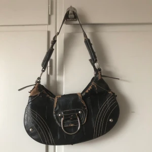 Baguette väska - Väldigt fin svart handväska. Rätt så sliten men har otrolig charm. Rymmer mer än vad man tror. Mobil,plånbok,hårborste,puder får utan problem plats! Jag har till och med fått ner en liten stickad kofta.