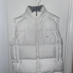 Vintage Nike väst - Vintage Nike pufferväst vit. Säljs inte längre. Väldigt bra skick. Fin och varm. Storlek L, passar bra på mig som är 186cm lång på bilden. Passar bra till storlek L men även som en oversized fit på storlek M. 