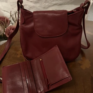 Röd axelremsväska - Knappt använd röd axelremsväska med tillhörande liten plånbok. Justerbar axelrem