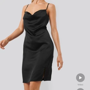 Svart klänning med slits  - Säljer denna oanvända svarta satin klänningen från NA-KD! Endast testad med prislappen fortfarande på! Köpt för 400kr o slutsåld på hemsidan, säljer pga för stor annars jätte fin klänning! Frakt tillkommer <3
