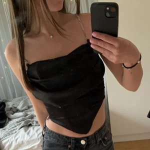 Festtopp i sidenmaterial - Svart festlinne i korsettliknande och med extra tyg vid bysten💓 Toppen är i väldigt fint glansigt sidenmaterial. Man kan ha den med glitterband men också utan. Den sitter tajt så ingen risk att den åker ner om man har den utan band. Säljer pga. att den tyvärr inte används. Köptes från ASOS för 400 kr.