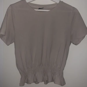 Beige topp med volang  - Beige topp från Gina Tricot med en volang nedtill, säljer på grund av att den inte kommer till användning.