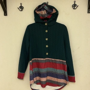 Härlig tröja i fina färger  - Härlig tröja med luva i fina färger. Fint skick. 5 knappar på bröstet.  Köparen står för frakten. Jag ansvarar inte för postens hantering. Jag visar bild på när jag skickar paketet. Vid fler intressen av objekt kan bud över begärt ingångspris läggas.