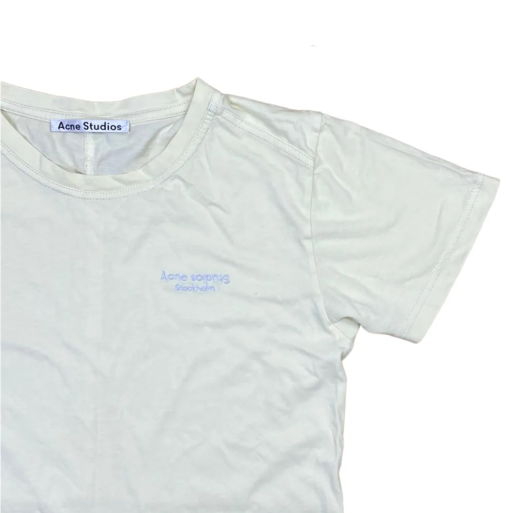 Acne T-Shirt i storlek Small, fråga för mått. Den är i pastell gul färg och har en ljusblå broderad Acne logga. Har tyvärr en stor fläck som syns på sista bilden.. T-shirts.