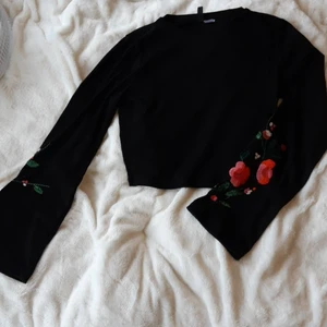 Croppad stickad tröja från HM - Svart croppad tröja. Utsvängda ärmar med broderi föreställande blommor🌺Använd en gång.
