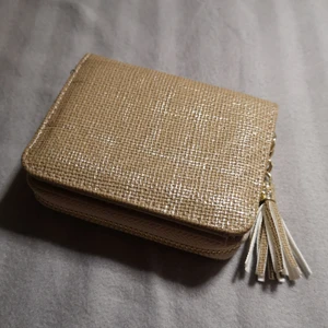 Plånbok  - En guld beige plånbok. Du kan förvara dina kort och sedlar i den, mynt är lite svårare med det går att ha i dragkedjan. Använd men inte utnöt, i ett väldigt fint skick. 
