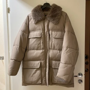 Beige vinterjacka - Snygg beige vinterjacka med fuskpälskrage från Asos. Inköpt förra året men är väldigt sparsamt använd.