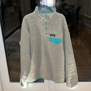 Patagonia fleece  - Beige/gråfärgad fleece med turkosa detaljer från Patagonia. I mycket bra skick, använd ett fåtal gånger bara.  