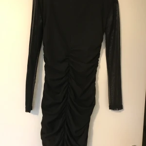 Draperad klänning - Svart klänning draperad bak med mesh-ärmar i nyskick, stl S. Frakt betalas av köparen.