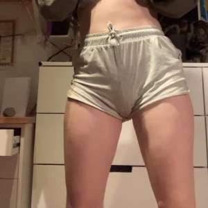Tygshorts m snören - 90% bomull, 5% viskos, 5% elastan. Grå shorts i tyg med resårmidja och snören för att justera hur byxorna sitter. Detalj med snören dragna genom metallringar på sidorna. Några år gamla men hela och rena. 