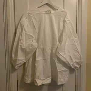 Cos blus öppen rygg - Vit, krispig blus från COS med öppen rygg och knyt i nacken stora puffiga ärmar. Ostruken i bild och det är så jag använt den. Jag har använt den som väldigt oversized men skulle tro att den är stor även för en 44. Fint skick pga sparsamt använd.