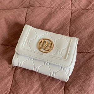 Plånbok från river island🫶🏼 - Vit och fin plånbok från River island. Det står RI runt hela plånboken och har ett stort guldigt tryck fram på plånboken:) jag köpte den förra året och har används många gånger men är i bra skick. Den har gått sönder lite vid ytter facket!💗