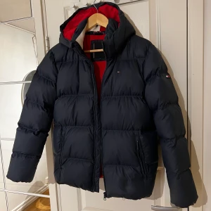 Tommy puffer jacket  - puffer jacket som är väldigt varm köpt för 2400kr helt oanvönd passar perfekt för vintern. Luvan går och ta av om man önskar. Färgen är mörk blå med snygga röda detaljer inuti. Passar både killar och tjejer. Skriv vid intresse. Köparen står för frakten 🤍 