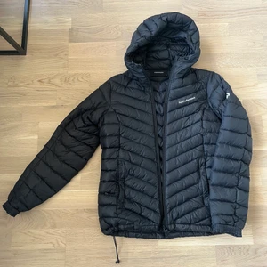 Peak Performance - En svart dunjacka från Peak Performance.  Jackan är 1.5 år gammal. Jackan har luva  samt en fick på varje sida som stängs med dragkedja. Jackan har dragsko för önskad passform nertill. Storlek M. 