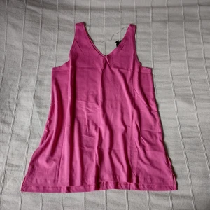 Oanvänt rosa/cerise v-ringat linne, storlek S - Oanvänt a-linjeformat och v-ringat linne i en jättefin rosa färg. En söm mitt i fram och en i bak. Kort sprund i sidorna och en liten längre bakdel. 100% bomull. Ca 70 cm långt. Storlek S. Frakt 30 kr. 