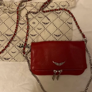 Zadig väska röd💋 - Nu säljer jag min fina röda Zadig väska då den inte kommer till lika mycket användning längre. Väskan är i jätte bra skick och knappast använd. Dustbag medföljer men tyvärr inget kvitto då jag tappat bort det. Kan garantera att den är äkta. Säljer inte under 850kr men kan även tänka mig byta mot någon annan väska.💋