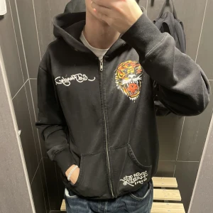 Ed hardy - Säljer min svinfeta ed hardy zip up då den inte används. Zippen är trasig, alltså går den öppna men inte stänga (används som vanlig hoodie). Tröjan är i bra skick endast tappat några rinestones. Därav schysst pris!