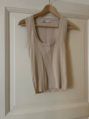Beige ribbad linnetopp från Zara - Säljer en beige ribbad linnetopp från Zara med breda axelband och rundad halsringning. Toppen är ärmlös och har en enkel, stilren design som passar perfekt till alla dina outfits.