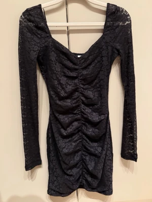 Svart spetsklänning  - Snygg svart kort klänning i spets med långa ärmar. Klänningen har en djupare urringning och är figurnära i modellen. 