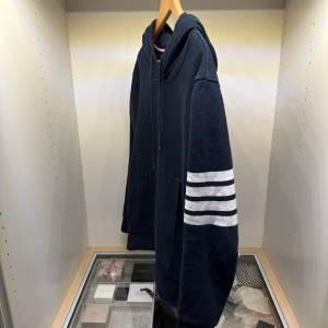 Thom Browné Hoodie ~ 4 Bar - 🔷 Mörkblå hoodie i klassisk design 🔷 Ikoniska 4-bar ränder på ärmen (signatur för Thom Browne) 🔷 Mjuk bomullskvalitet (ser ut som sweatshirt-material) 🔷 Kangaroo pocket framtill 🔷 Ribbad nederkant och muddar 🔷 Hood med snörning 🔷 Minimalistisk och clean look 🔷Storlek M                                                                                 🔷OBS!! Inga tags 