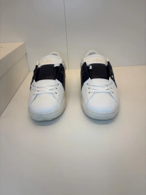 Valentino Opens - Säljer ett par stilrena Valentino Garavani sneakers i vitt med marinblå detalj, storlek 43. Tidlös modell som passar till allt. Använda med normalt slitage på sulan (se bilder), men i fint skick i övrigt. Originalbox och kvitto medföljer. Äkta vara – bra pris jämfört med nypris! ✨