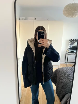 Svart dunväst med huva - Säljer en svart dunväst med beige insida och stor huva. Västen har en oversized passform och stängs med dragkedja och knappar. Perfekt för lager på lager och riktigt snygg till jeans eller hoodie.🤩Nypris 600kr