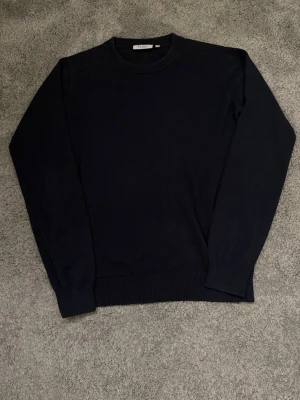 Mörkblå stickad tröja med rund hals - Stilren mörkblå tröja köpt från NK i Stocholm 170-176 passar till allt, hör av er vid frågor!