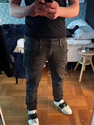 Replay jeans - Säljer ett par Replay Anbass jeans i svart tvätt med snygga slitningar och klassiska fem fickor. Jeansen har en slim passform och raka ben, med detaljerade sömmar och Replay-logga på bakfickan. Snygg tvättad look! Skriv vid fundering!