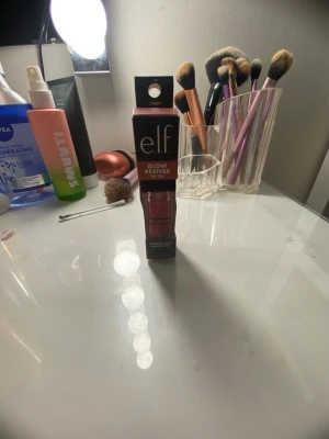 e.l.f. Glow Reviver Lip Oil rosa - Säljer ett e.l.f. Glow Reviver Lip Oil i en snygg rosa nyans. Kommer i en stilren fyrkantig tub med svart lock och genomskinlig flaska som visar färgen. Innehåller aprikoskärnolja för extra glans och vård till läpparna.