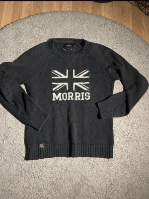 Morris stickad tröja med Union Jack - Säljer en mörkgrå stickad tröja från Morris med Union Jack och Morris-logga i vitt på bröstet. Tröjan har rund halsringning, ribbade muddar och är tillverkad i mjukt material som passar perfekt för kalla dagar och riktigt skön stil. Skriv om frågor! 