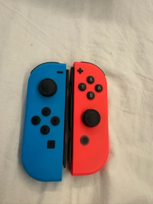 Nintendo Switch med blå och röd Joy-Con - Nintendo Switch spelkonsol med en blå Joy-Con till vänster och en röd Joy-Con till höger. Konsolen har en stor skärm i mitten och avtagbara handkontroller. Perfekt för gaming både hemma och på språng. Klassisk design och smidigt format. Knappt använd, bara haft den ståendes utan användning, den kommer med dosan, hdmi kabel och laddare 